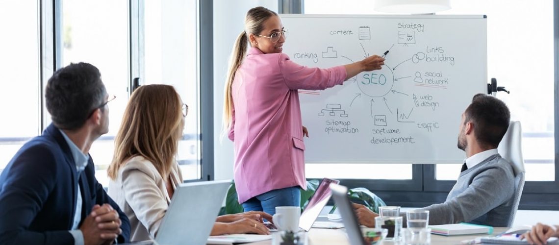 Shot of elegant young businesswoman pointing at white blackboard and explain a project to her colleagues on coworking place.