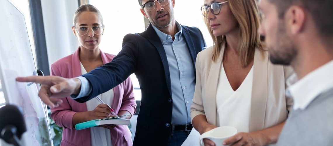 Shot of handsome businessman pointing at white blackboard and explain a project to her colleagues on coworking place.
