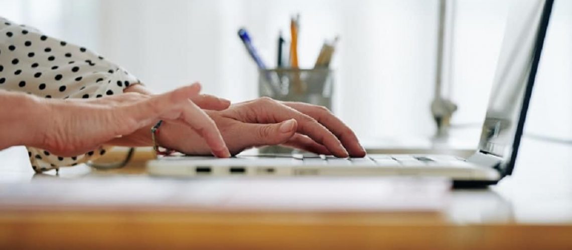 Hands of female entrepreneur working on laptop at her office table, answering e-mails from partners and clients